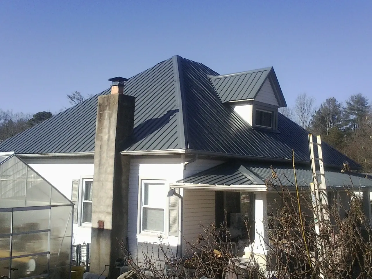 Dark blue standing seam metal roof on a white farmhouse with dormer — Slate & Tile Roof Repair by Roofing Brothers in Whitney Point