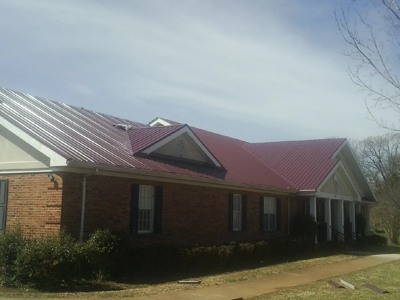 Red metal roof with gabled entries on a long brick building, from a Hail Damage Roof Repair job in Whitney Point