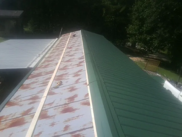 Old rusted panels beside newly installed green metal roofing — Wind Damage Roof Repair by Roofing Brothers in Whitney Point