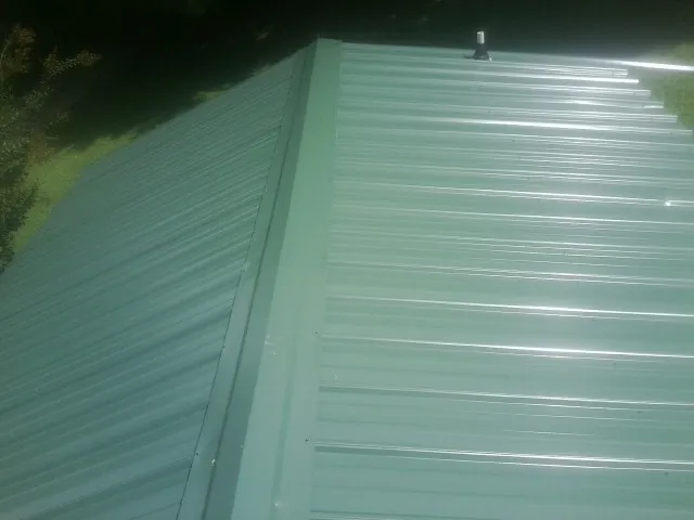 New green metal panels meeting at the ridge of a roof — Flat Roof Repair work by our crew in Whitney Point