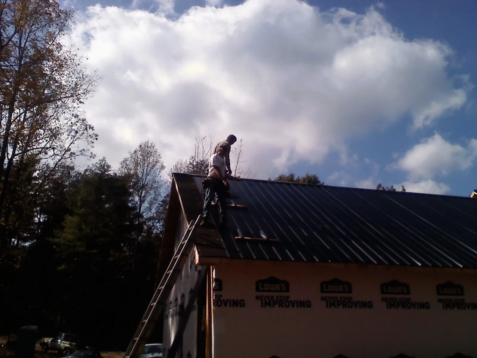 Roofer fastening dark metal panels high against a cloudy sky, from a Roof Inspection job in Whitney Point