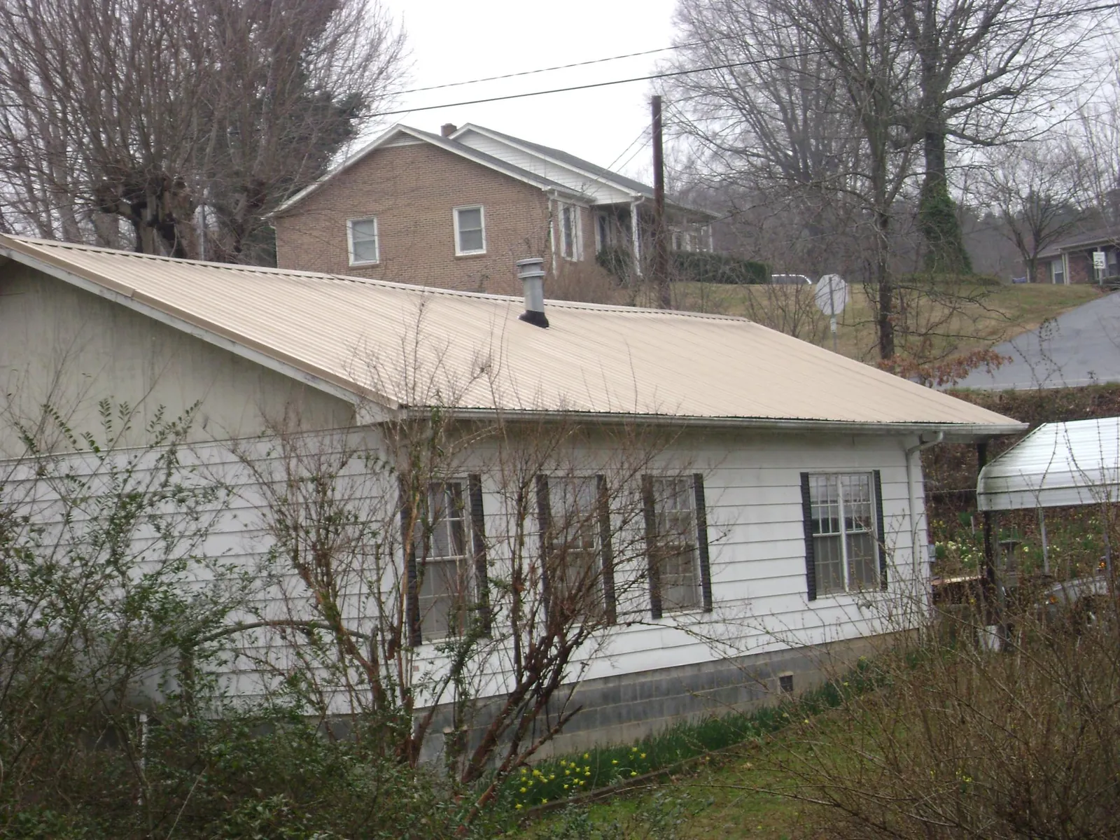 Tan metal roof on a white sided house set into a hillside — Commercial Roofing by Roofing Brothers in Whitney Point