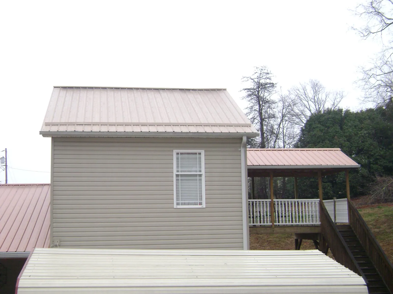 Tan metal roofs on a two story addition and attached porch, from a Roof Replacement job in Whitney Point
