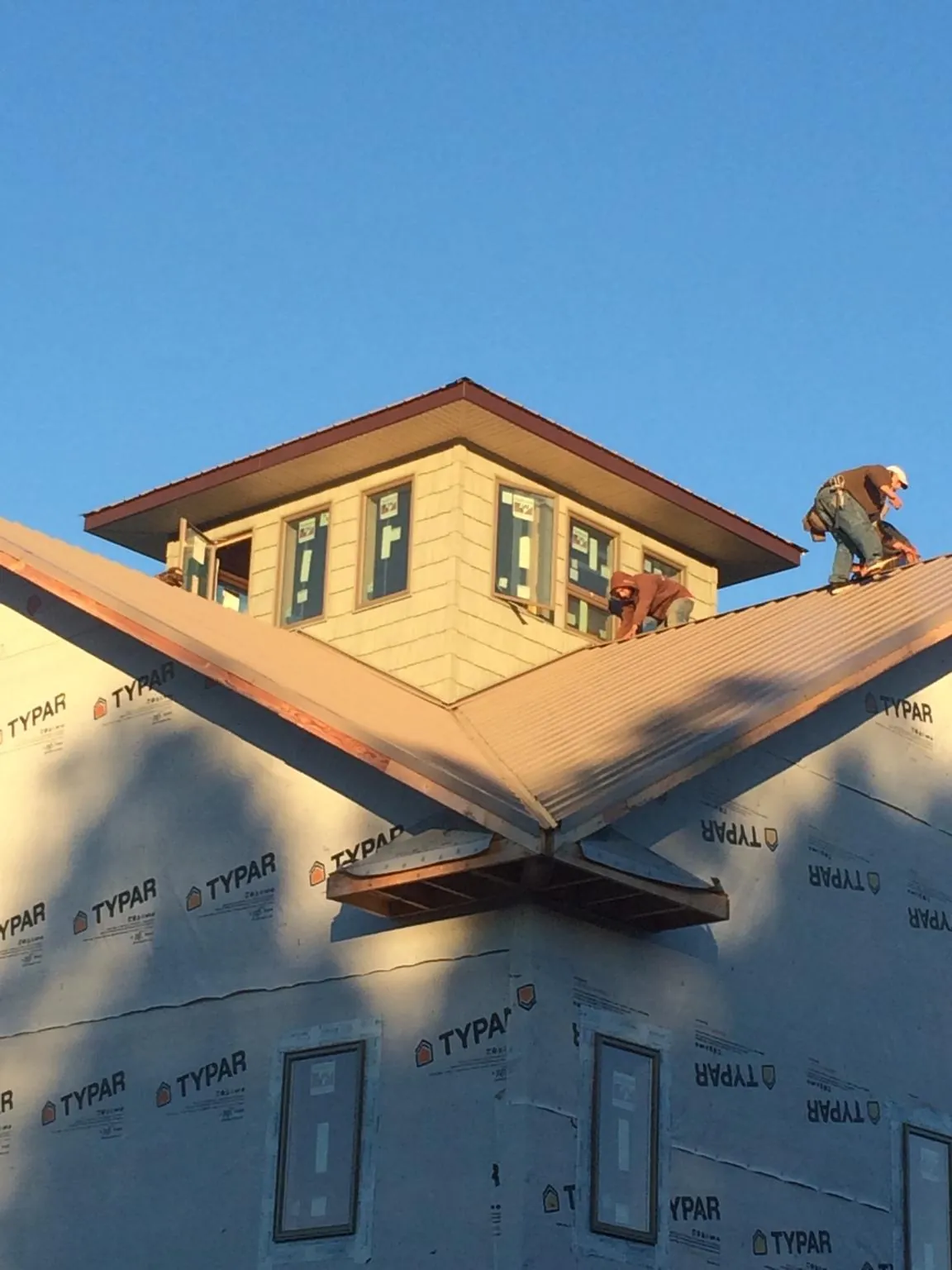Roofers working around a rooftop cupola on a new metal roof at sunset — Roof Waterproofing in Whitney Point by Roofing Brothers